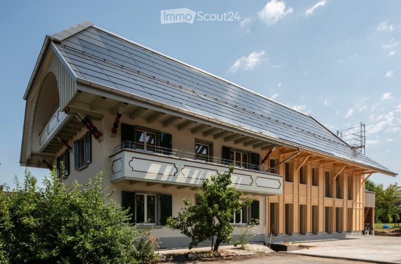 Modern two-story building with a large balcony, metal roof, and wooden facade elements.