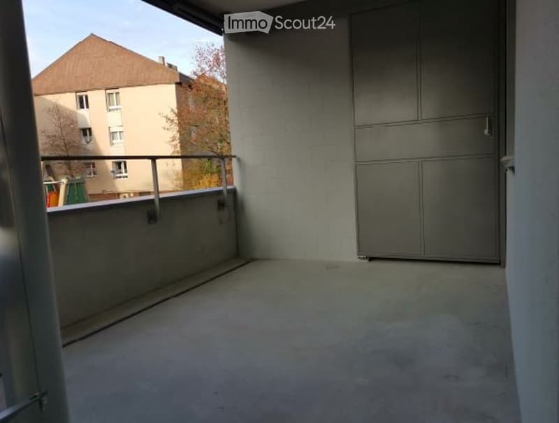 Empty balcony with concrete floor, metal railing, grey cabinets, and view of neighboring building.