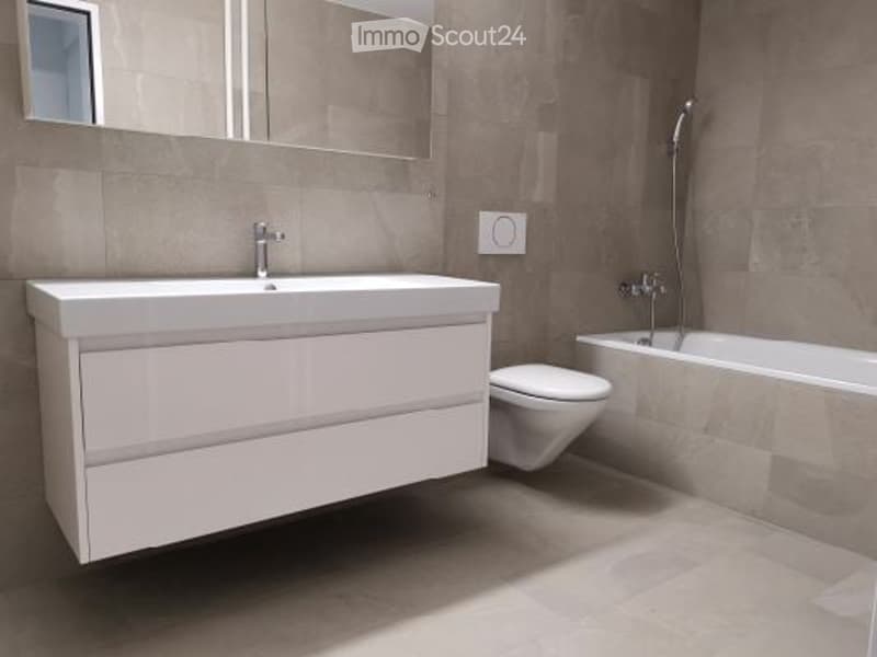 Modern bathroom with a white sink, toilet, bathtub, and large mirror. The walls and floor are tiled in a neutral color scheme.