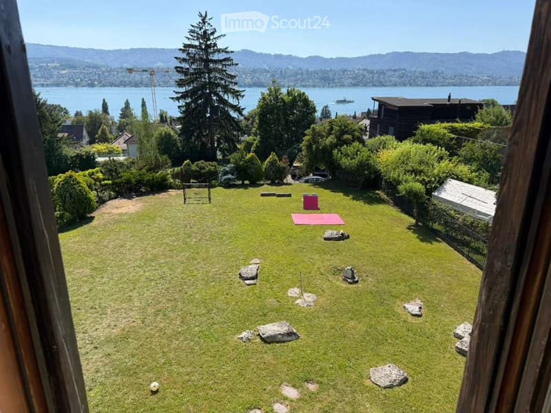 Lush green garden with scattered rocks, a yoga mat, a small table, and a view of a lake and distant mountains.