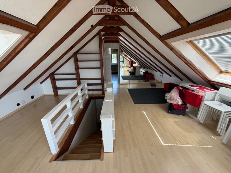 Attic space with wooden beams, wooden flooring, white railing, and a small seating area with chairs and a table.
