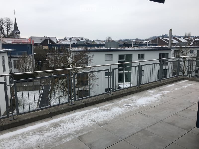 Outdoor area with tiled floor and railings, overlooking the city, and snow on the ground