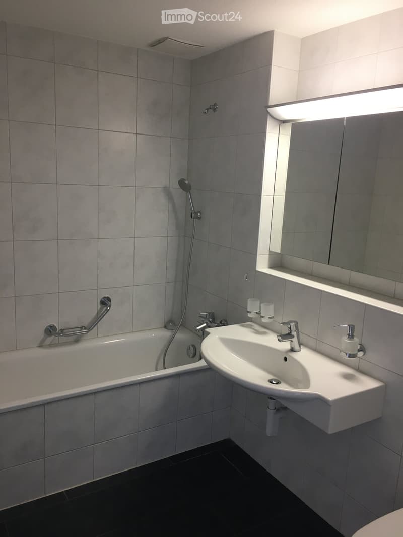 white tiles, white bathtub, white sink, showerhead, mirror with shelf