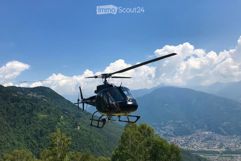 A helicopter flying over a mountainous landscape with a town visible in the distance.