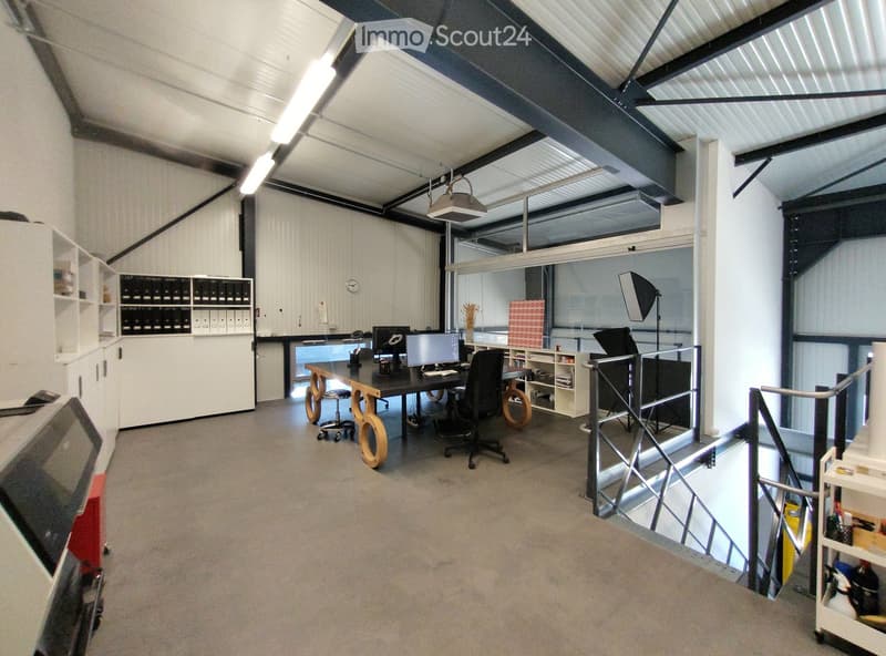 Modern office space with a large desk, multiple chairs, computer setup, shelves, and a staircase leading to another level.