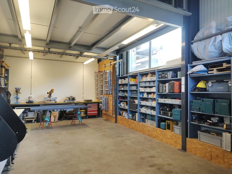 Workshop area with large windows, metal shelving units filled with tools and supplies, a workbench with tools, and storage bins.