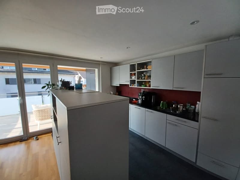 Modern kitchen with white cabinets, dark countertops, and a central island. Features include a coffee maker, cups, and a small plant on the counter.