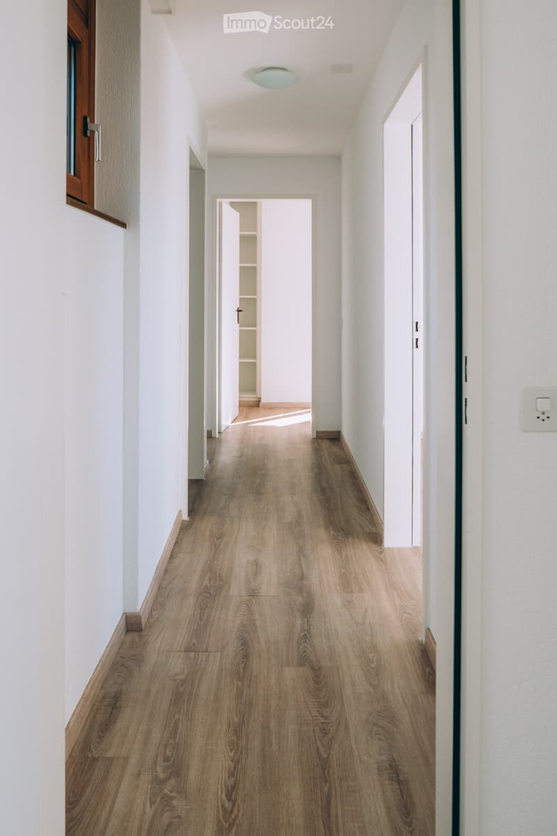 Clean, modern hallway with light wooden flooring, white walls, and several open doors leading to other rooms.