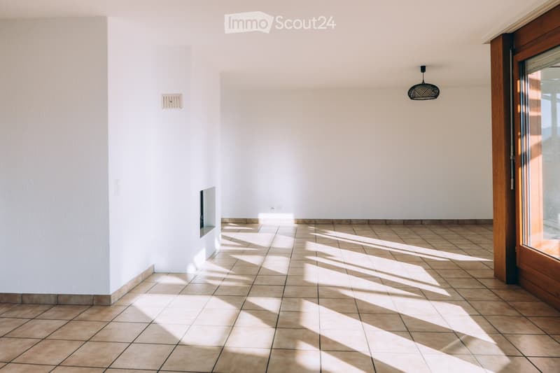Empty room with tiled floor and white walls, featuring a hanging light fixture and a wooden door with glass panels.