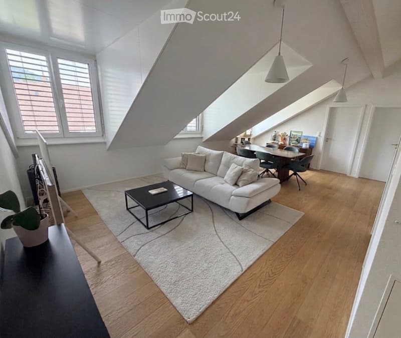 Modern living room with white sofa, black coffee table, dining area with table and chairs, pendant lights, and large windows with blinds.