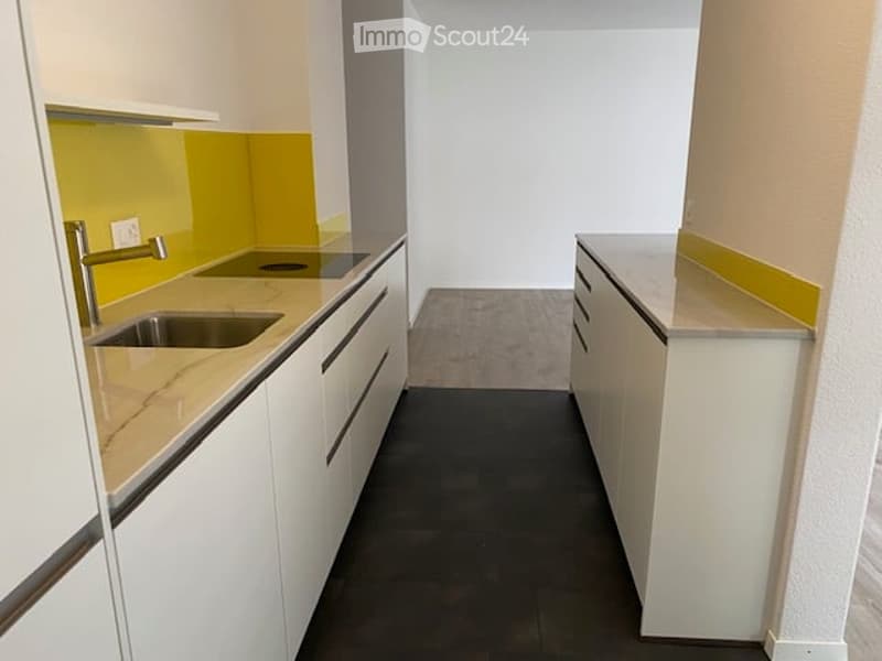 Modern kitchen with white cabinets, marble countertops, and a stainless steel sink. The backsplash is yellow, and the floor is dark.