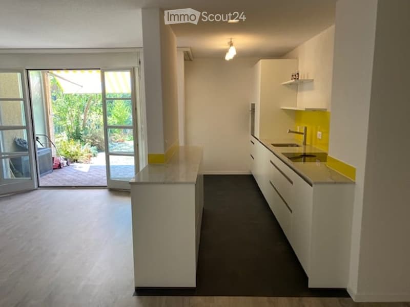 Modern kitchen with white cabinets, a central island, and a sink. The space features large windows and a sliding glass door leading to an outdoor area.