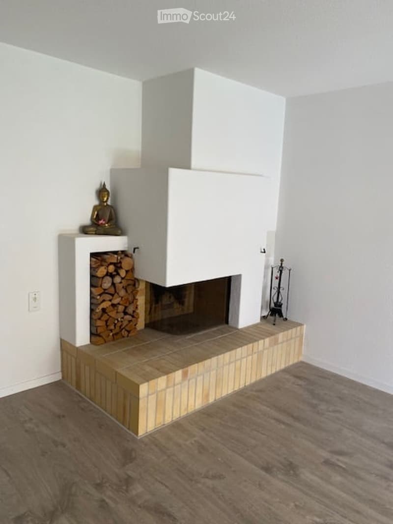 Modern fireplace with white surround and tiled base, wood stack to the left, decorative statue, and fireplace tools to the right.