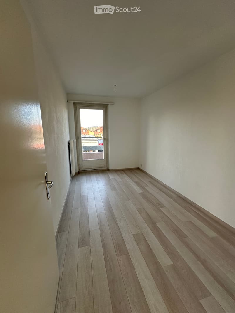 Empty hallway with wooden flooring, white walls, and a door leading outside.