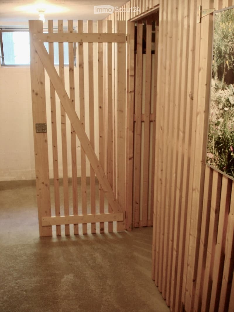 Empty hallway with wooden panel walls, a large wooden gate, and a small window letting in natural light.