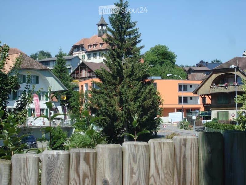 A view of a small town with a mix of residential and commercial buildings, including a prominent clock tower, surrounded by trees and greenery.