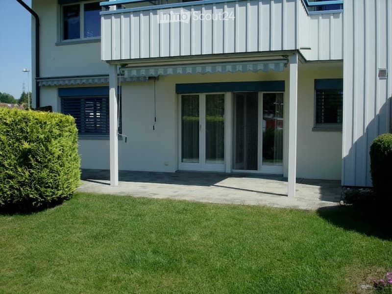 Two-story white building with a balcony, large windows, and a well-maintained lawn in front.