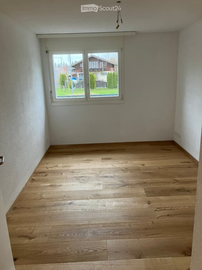 Empty room with wooden flooring and large windows showing a view of the outside. No furniture or equipment present.