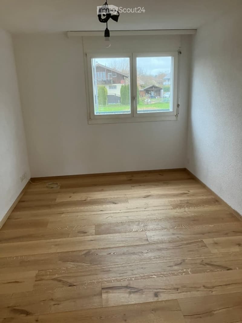 Empty room with wooden flooring and large window, no furniture or equipment present.