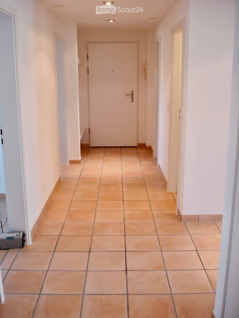 Empty hallway with tiled floor, white walls, and a closed door at the end.