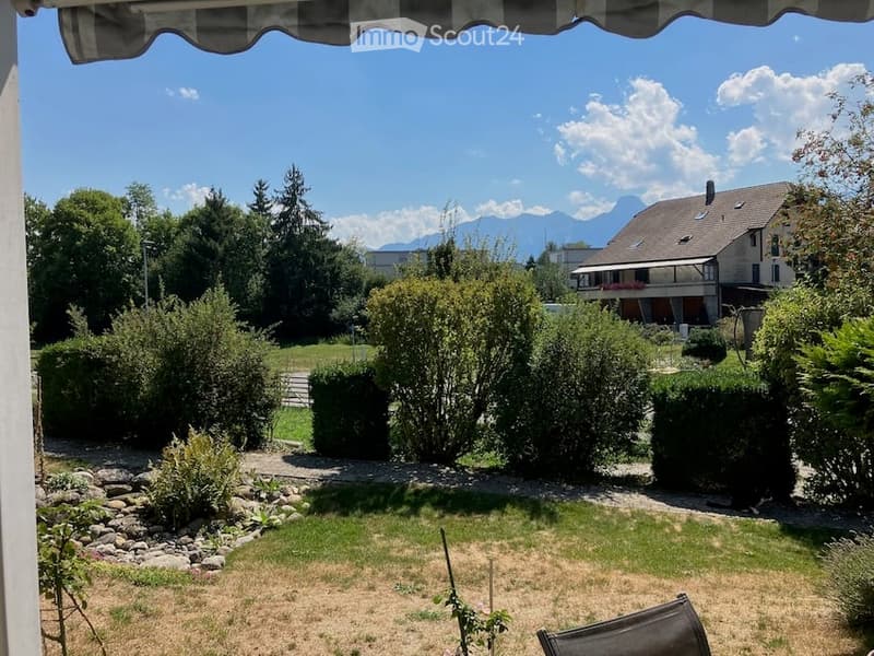 Garden with trimmed bushes, a gravel pathway, and a view of a house and mountains in the background.