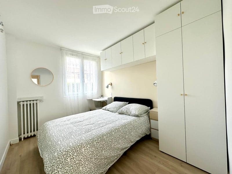 Cozy bedroom with a double bed, nightstand, mirror, radiator, desk, chair, and built-in cabinets.