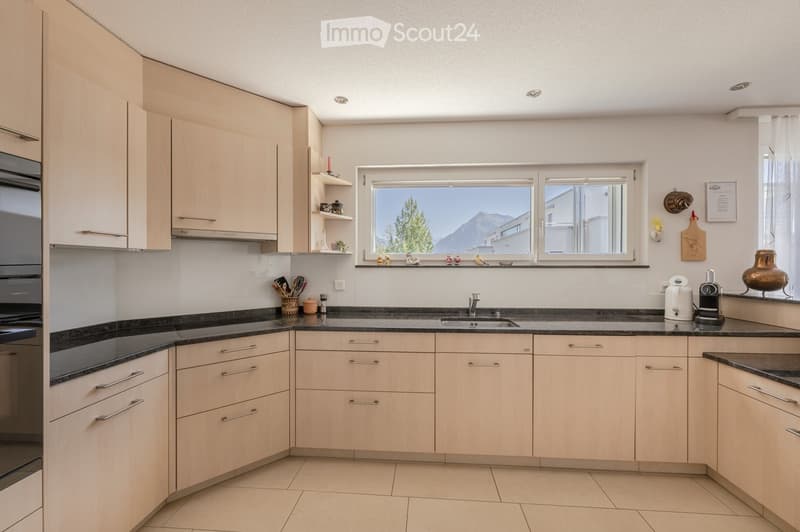 Modern kitchen with light wood cabinets, black granite countertops, stainless steel appliances, and a window overlooking a scenic mountain view.