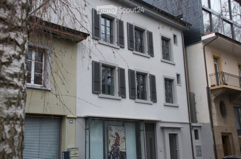 A multi-story residential building with white walls, multiple windows with shutters, and a closed garage door on the ground floor.