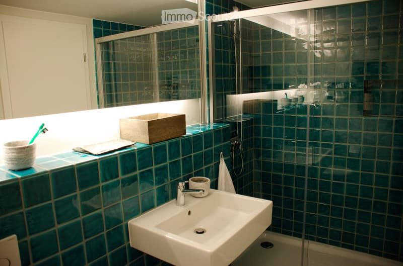 Modern bathroom with teal tiles, white sink, glass shower enclosure, and decorative wooden box on the counter.