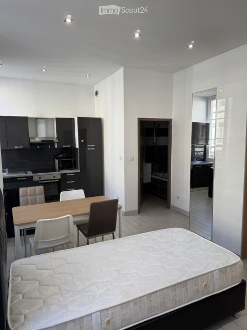 A modern, open-plan living space with a bed, dining table, chairs, and a fully equipped kitchen area featuring cabinets, a microwave, and a refrigerator.