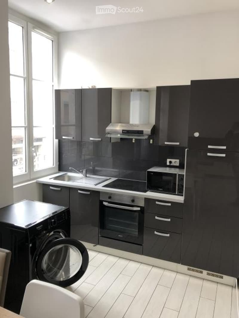 Modern kitchen with black cabinets, stainless steel appliances, and white tiled flooring.