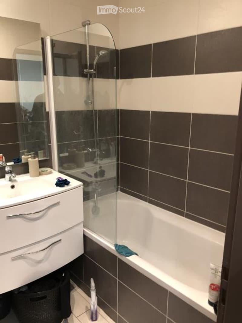 Modern bathroom with white sink, mirror, bathtub, and glass shower enclosure. Dark brown tiles on walls and floor.