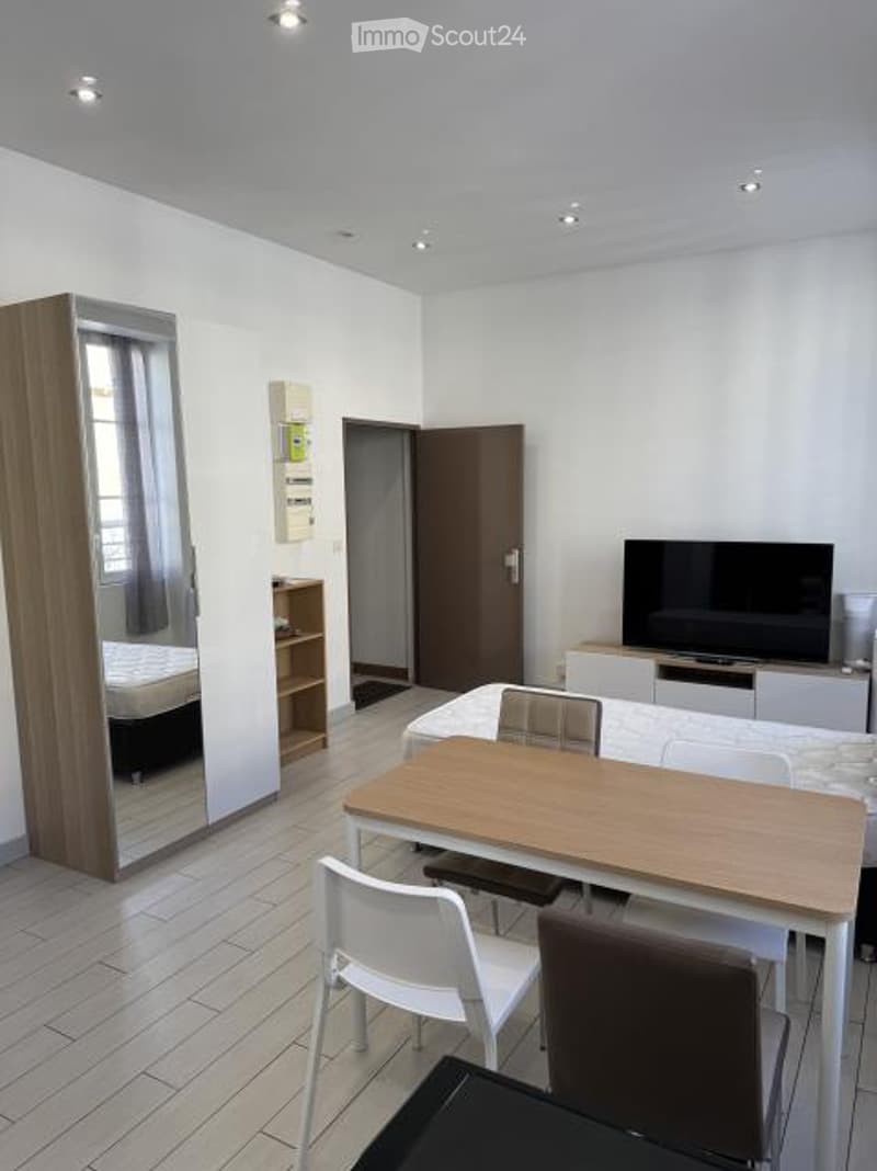 A modern, well-lit room with a large mirror, a wooden table with chairs, a TV on a stand, and a shelf with various items.