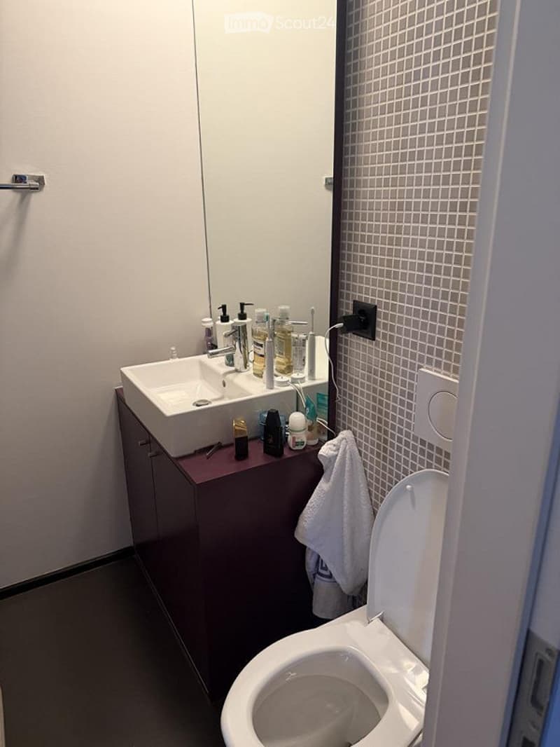 Modern bathroom with a white sink, faucet, and toilet. A dark-colored cabinet holds various toiletries, and a white towel hangs on the side.