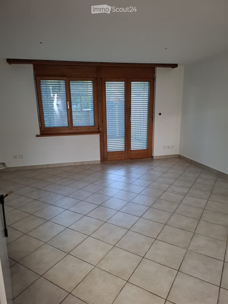 Empty room with tiled floor, large window with blinds, and neutral-colored walls.