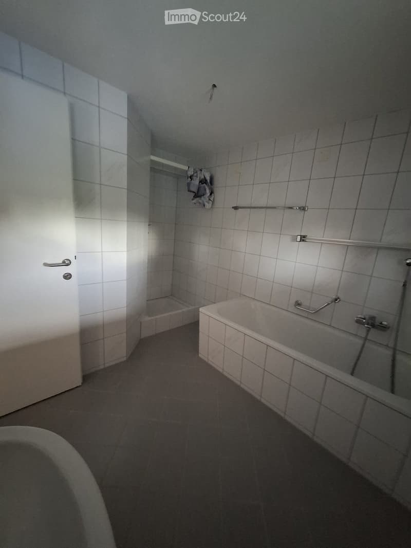 A small bathroom with a bathtub, tiled walls, a door, and a handrail for support.