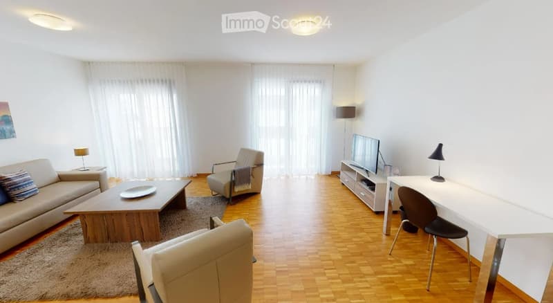 Modern living room with light wooden flooring, large windows with white curtains, a sofa, coffee table, armchairs, TV stand, and a desk with a chair.