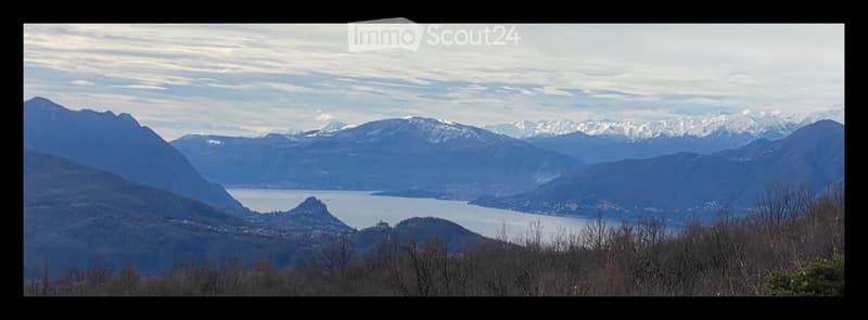 Panoramic view of a lake surrounded by snow-capped mountains and a town in the distance.