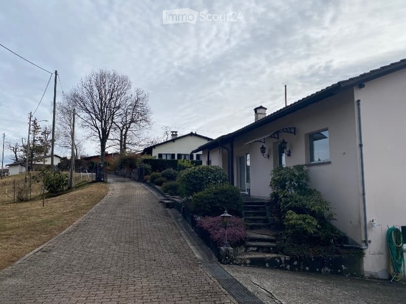 A two-story house with a modern facade, surrounded by well-maintained gardens and a paved driveway.