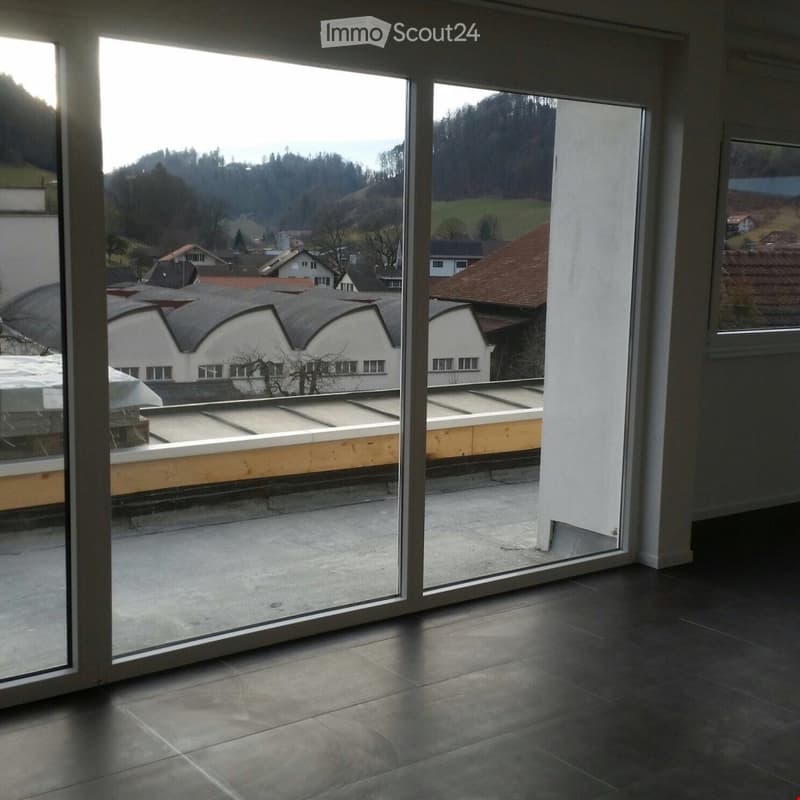 Large balcony with expansive view of surrounding landscape and buildings, modern glass sliding doors, dark tiled floor.