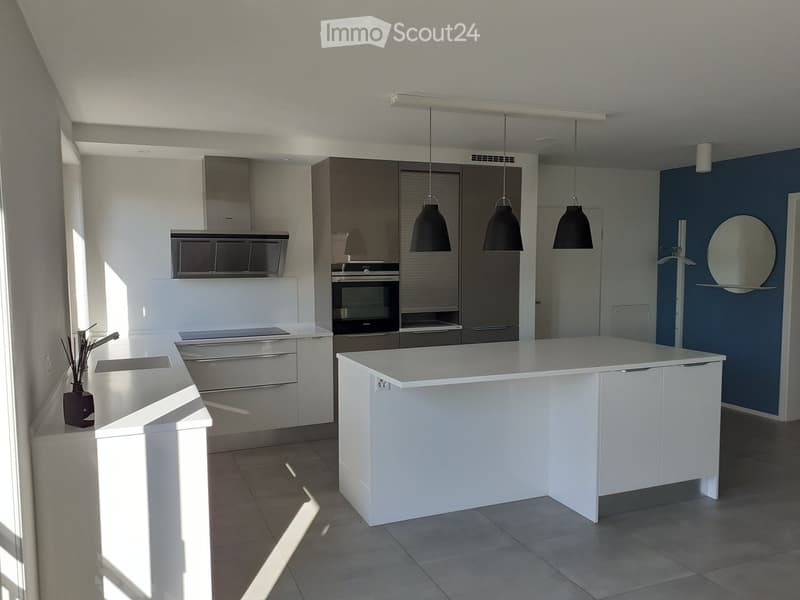 Modern kitchen with white cabinets, island, sink, oven, and pendant lights.