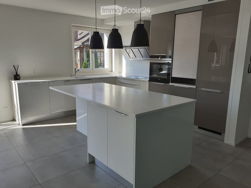 Modern kitchen with white cabinets, stainless steel island, sink, oven, refrigerator, and pendant lights.