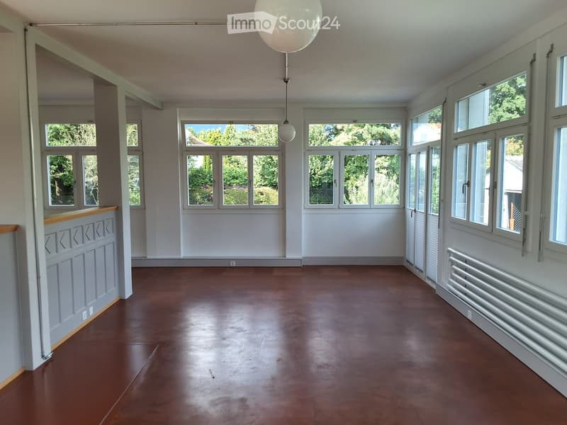 Empty room with wooden floor, large windows, and a decorative wooden panel on one wall.