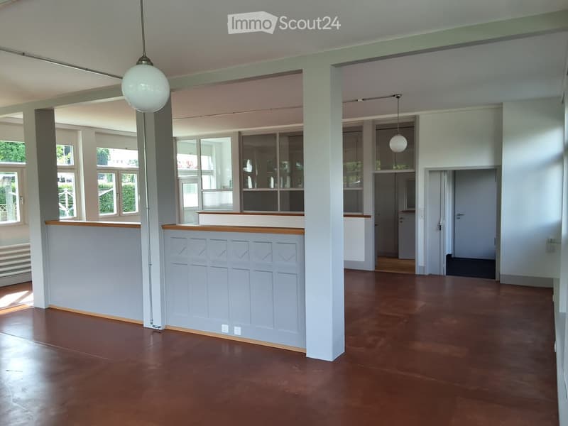 Empty room with wooden flooring, white walls, large windows, and decorative paneling. No furniture or equipment present.