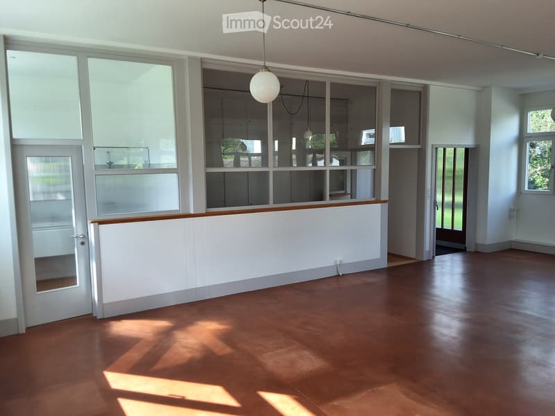 Empty room with wooden flooring, white walls, large windows, and a hanging light fixture. No furniture or equipment present.