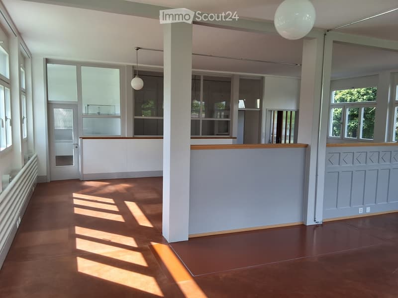 Empty room with wooden flooring, white walls, large windows, and a central column. No furniture or equipment present.