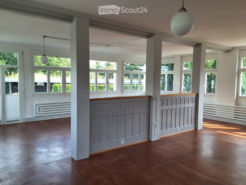 Empty room with wooden flooring, large windows, and decorative paneling on the walls.