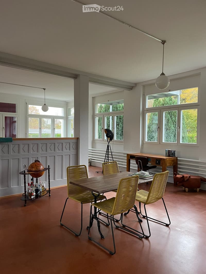 Bright, open room with large windows, wooden table, four chairs, globe on a stand, and a desk with office chair.