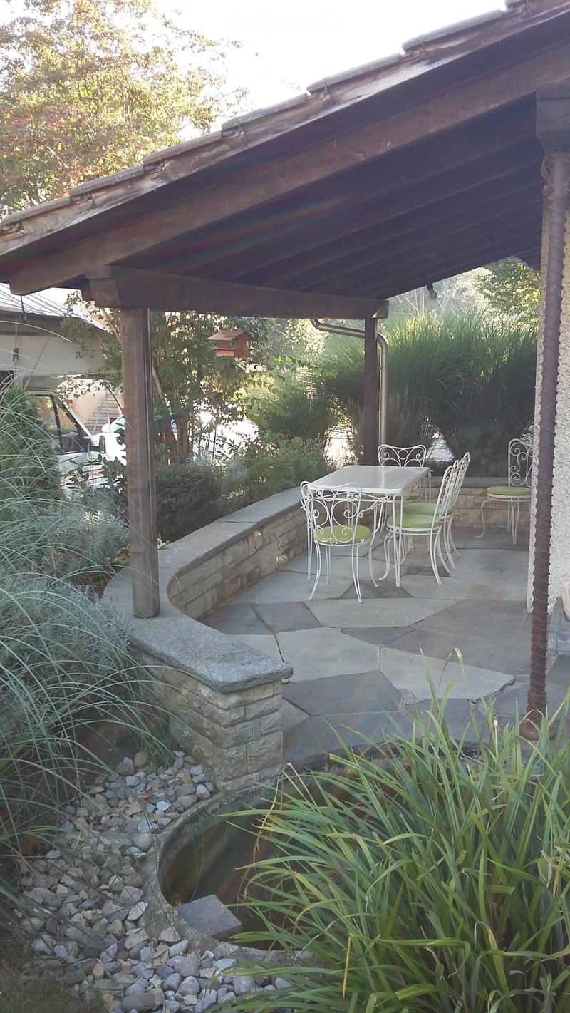 A covered outdoor patio with a stone wall, a small water feature, and a table with chairs.