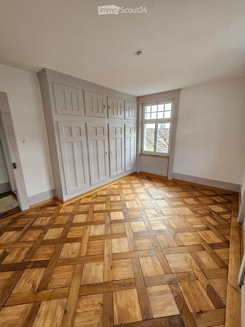 white walls, wooden parquet floor, large white built-in wardrobes, small window